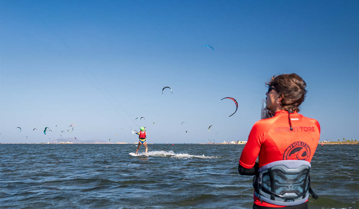 Kitesurfing instructor watching students practice kite control on the water during a beginner lesson.