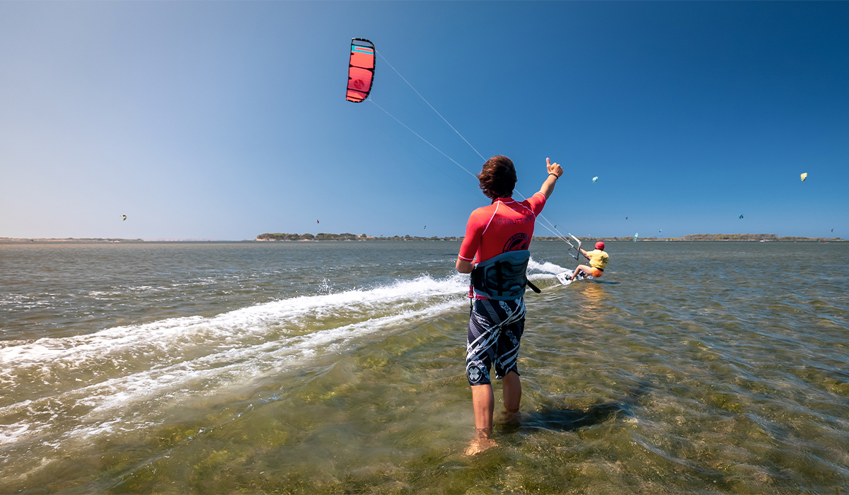 Kitesurfing instructor giving a thumbs-up to a student riding past during a beginner kitesurfing lesson.